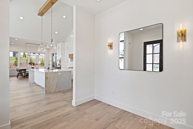 kitchen with a center island with sink, white cabinets, a sink, modern cabinets, and light wood-type flooring