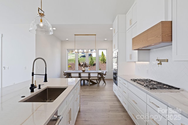 kitchen featuring stainless steel appliances, decorative backsplash, white cabinets, a sink, and light wood-type flooring