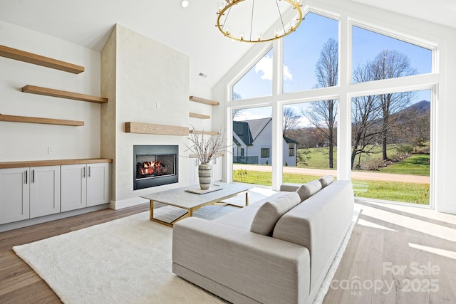 living room with a large fireplace, high vaulted ceiling, light wood finished floors, and an inviting chandelier