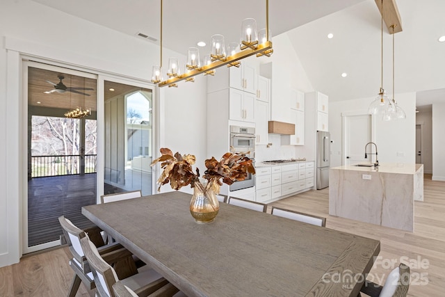 dining room with light wood-style floors, visible vents, a notable chandelier, and high vaulted ceiling