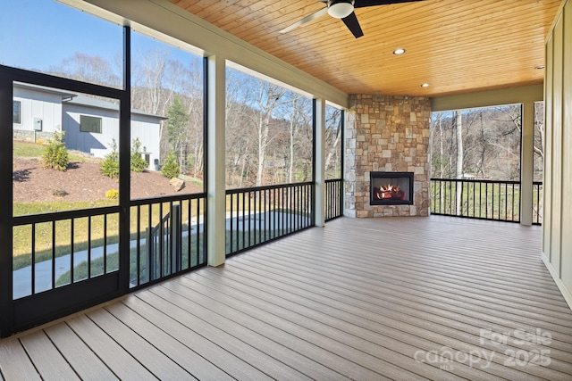 unfurnished sunroom with a ceiling fan, wood ceiling, and an outdoor stone fireplace