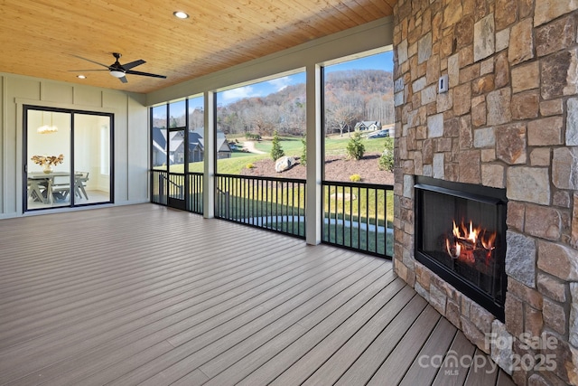 unfurnished sunroom featuring an outdoor stone fireplace, wooden ceiling, and a ceiling fan