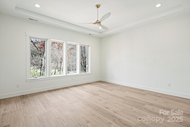 unfurnished room featuring a ceiling fan, light wood-type flooring, a raised ceiling, and baseboards