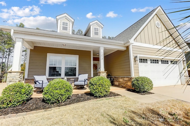 view of front of house featuring covered porch, board and batten siding, a garage, stone siding, and driveway