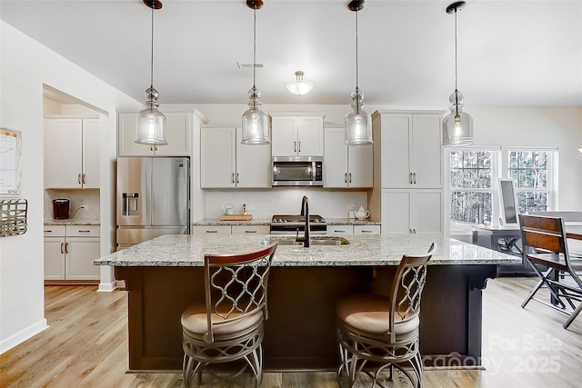 kitchen with light wood finished floors, visible vents, decorative backsplash, appliances with stainless steel finishes, and an island with sink