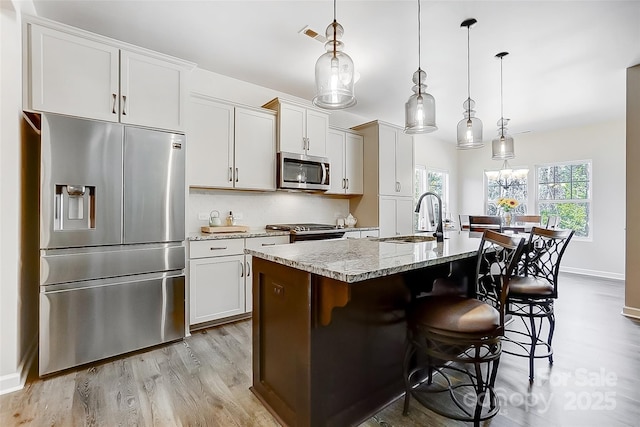 kitchen featuring a center island with sink, stainless steel appliances, a sink, light wood-type flooring, and a kitchen bar