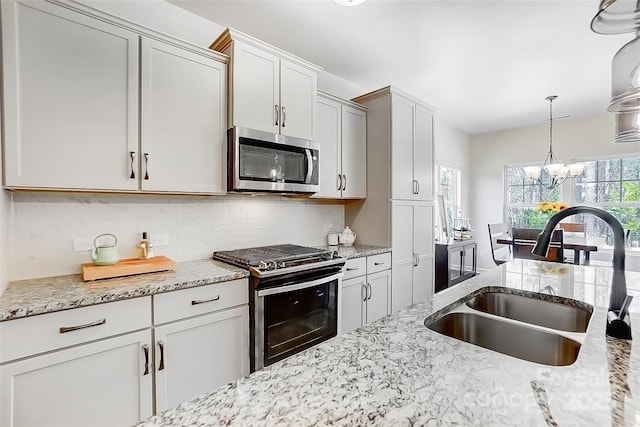 kitchen with appliances with stainless steel finishes, backsplash, a sink, pendant lighting, and a notable chandelier