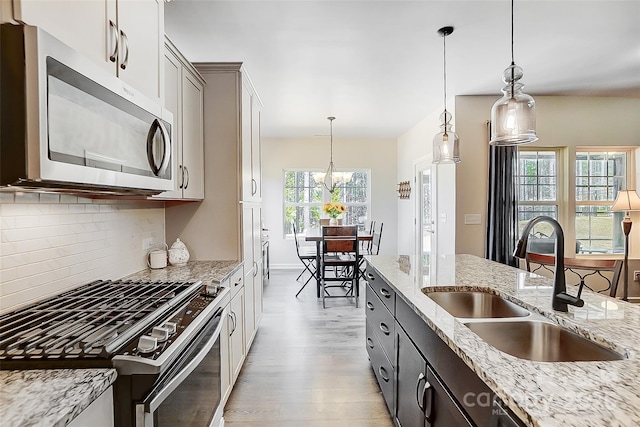 kitchen featuring decorative light fixtures, a sink, stainless steel appliances, light wood-style floors, and backsplash