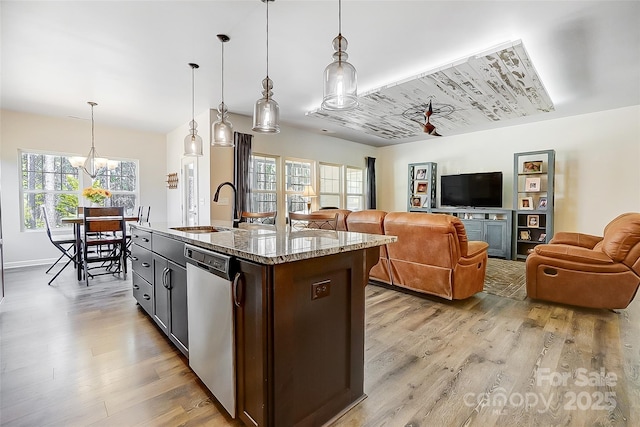 kitchen with dishwasher, light wood-style flooring, open floor plan, light stone countertops, and a sink