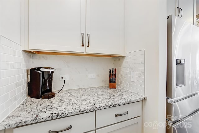 kitchen featuring light stone counters, white cabinetry, stainless steel refrigerator with ice dispenser, and decorative backsplash