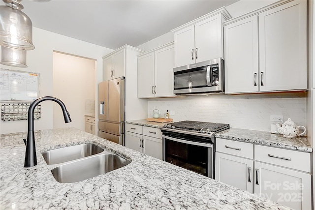 kitchen with tasteful backsplash, light stone countertops, stainless steel appliances, white cabinetry, and a sink