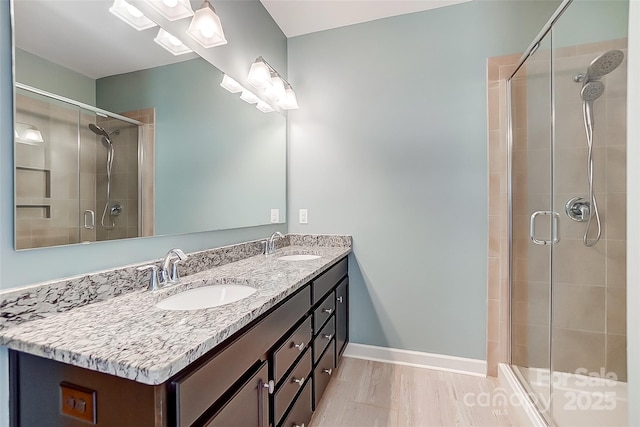 bathroom featuring baseboards, double vanity, a sink, and a shower stall