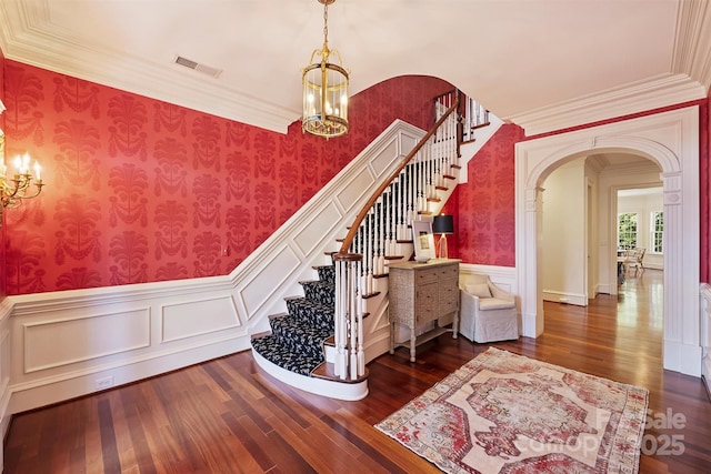 stairs with a chandelier, arched walkways, visible vents, and wallpapered walls