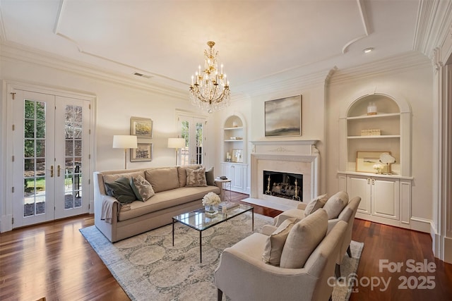 living room featuring built in features, french doors, crown molding, dark wood finished floors, and a fireplace with flush hearth