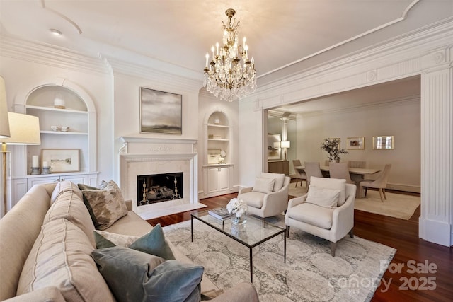 living room featuring built in features, dark wood-style flooring, an inviting chandelier, crown molding, and a high end fireplace