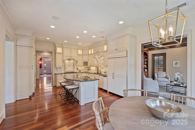 dining space with arched walkways, dark wood finished floors, visible vents, an inviting chandelier, and ornamental molding