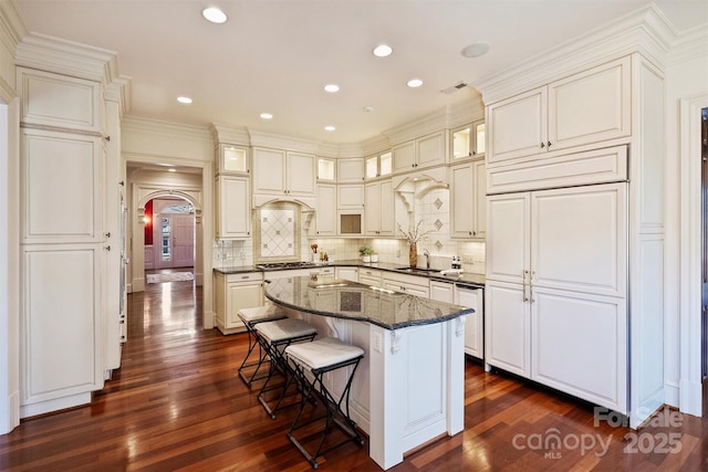 kitchen with a breakfast bar area, gas stovetop, decorative backsplash, a center island, and dark wood finished floors