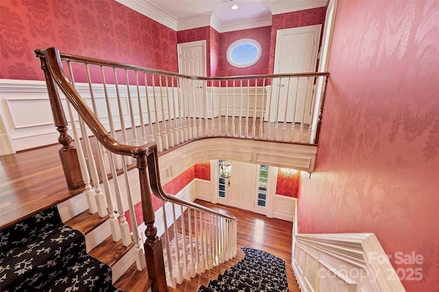 stairway featuring a decorative wall, a wainscoted wall, wood finished floors, wallpapered walls, and crown molding