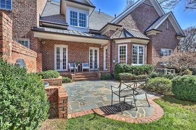 back of property featuring metal roof, a standing seam roof, french doors, a patio area, and brick siding