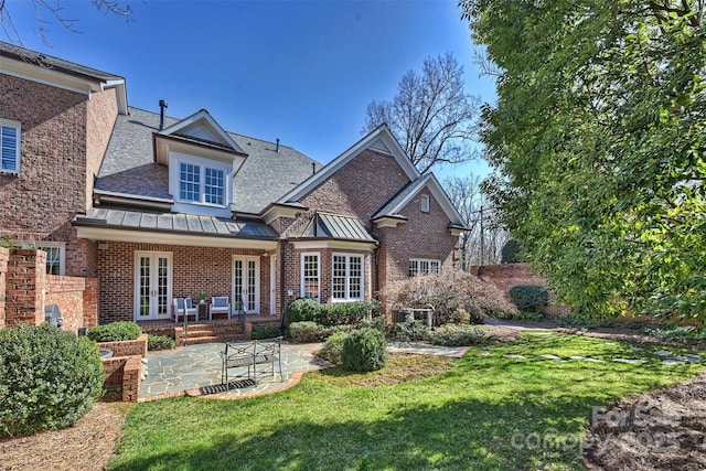 back of property featuring brick siding, french doors, a lawn, a standing seam roof, and a patio area