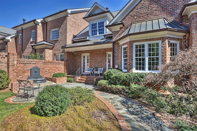 rear view of house with a standing seam roof, brick siding, fence, and metal roof