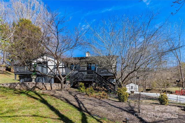 back of property featuring a chimney, a lawn, stairway, a deck, and driveway