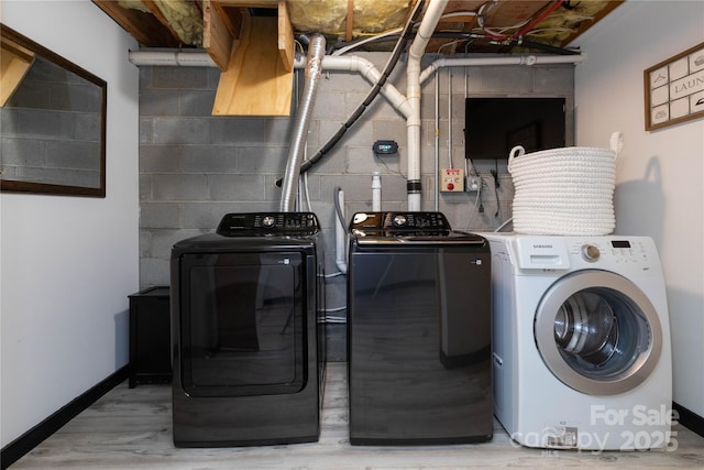 clothes washing area featuring concrete block wall, wood finished floors, laundry area, independent washer and dryer, and baseboards