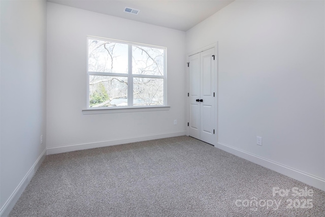 spare room with carpet floors, visible vents, and baseboards