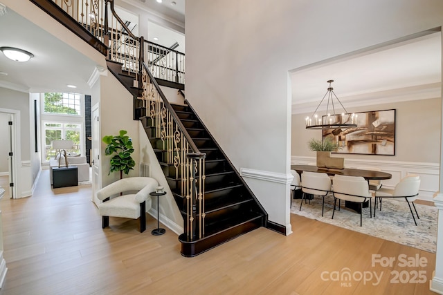 staircase featuring a towering ceiling, a wainscoted wall, ornamental molding, wood finished floors, and a chandelier