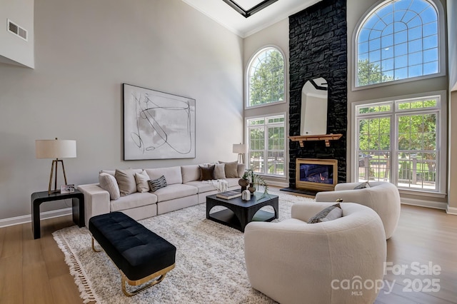 living area with crown molding, a fireplace, visible vents, a towering ceiling, and wood finished floors