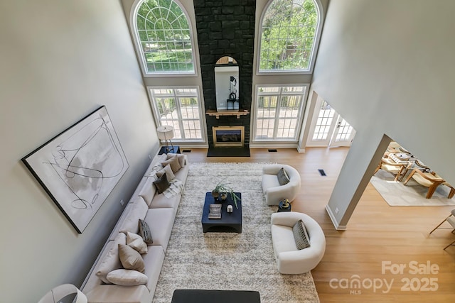 living room with a towering ceiling, a fireplace, visible vents, and wood finished floors