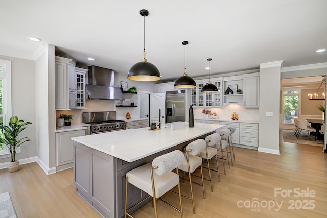 kitchen featuring wall chimney range hood, a large island, appliances with stainless steel finishes, and glass insert cabinets