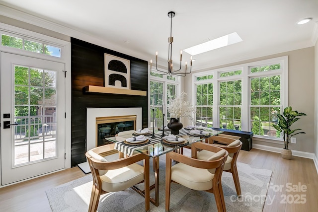 dining area featuring a large fireplace, crown molding, light wood-style flooring, and a healthy amount of sunlight