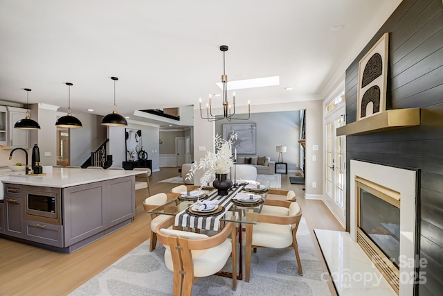 dining area with light wood-style flooring, a premium fireplace, stairway, an inviting chandelier, and crown molding