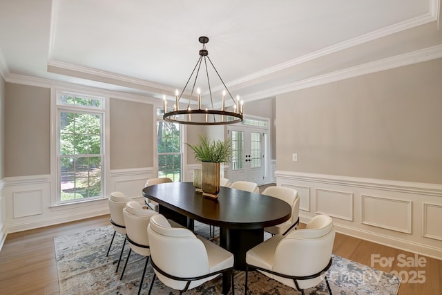 dining room featuring a wainscoted wall, french doors, a tray ceiling, and light wood-style flooring