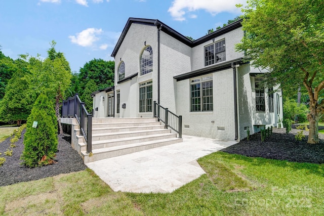 view of front of house with brick siding, crawl space, a patio area, and a front lawn