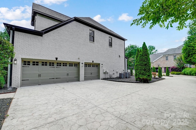 view of side of property with an attached garage, central air condition unit, driveway, and brick siding