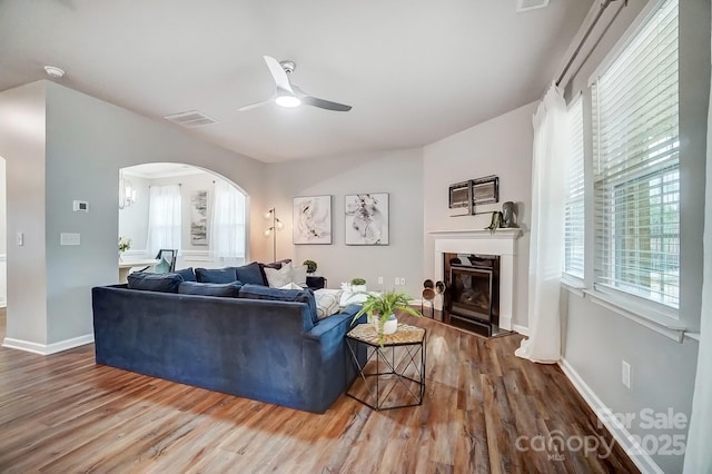 living area with a ceiling fan, visible vents, wood finished floors, and a glass covered fireplace