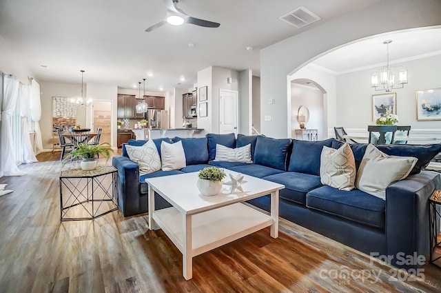 living room featuring visible vents, arched walkways, wood finished floors, crown molding, and ceiling fan with notable chandelier