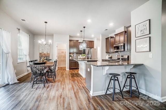 kitchen featuring a breakfast bar area, a peninsula, appliances with stainless steel finishes, light wood-type flooring, and dark stone countertops