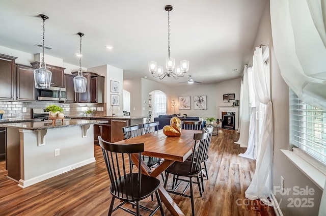 dining room with arched walkways, dark wood-style flooring, a glass covered fireplace, and visible vents