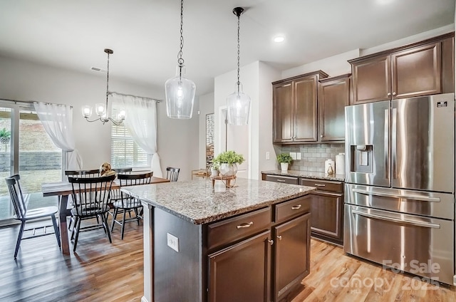 kitchen featuring pendant lighting, light wood finished floors, tasteful backsplash, light stone countertops, and stainless steel fridge with ice dispenser