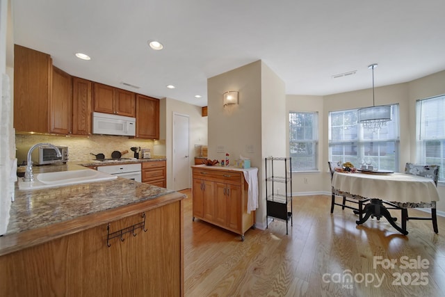 kitchen featuring brown cabinetry, pendant lighting, a sink, and white microwave