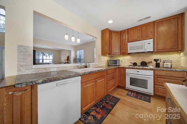 kitchen featuring visible vents, decorative backsplash, brown cabinetry, a sink, and white appliances