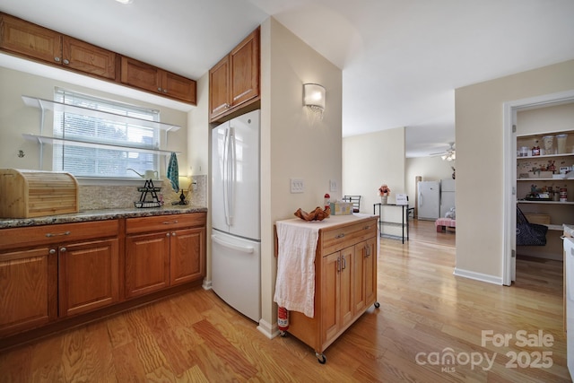 kitchen featuring light wood-type flooring, freestanding refrigerator, brown cabinets, and light stone countertops