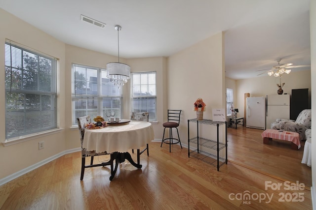 dining area with light wood-type flooring, visible vents, baseboards, and ceiling fan with notable chandelier