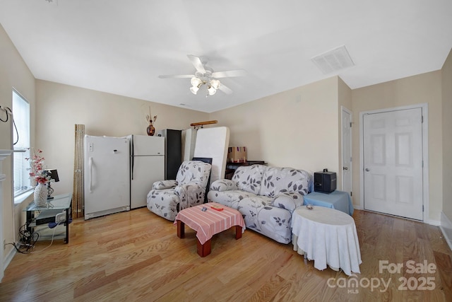 living room with light wood finished floors, visible vents, and a ceiling fan