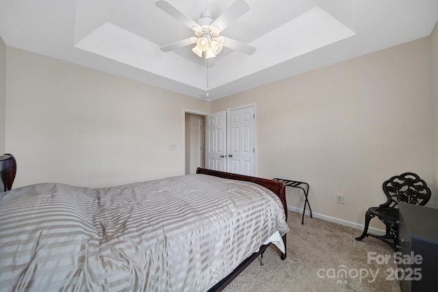 bedroom featuring a skylight, baseboards, a raised ceiling, a ceiling fan, and light colored carpet