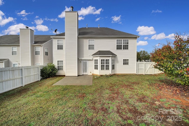 back of property with a patio, a fenced backyard, a chimney, a gate, and a yard