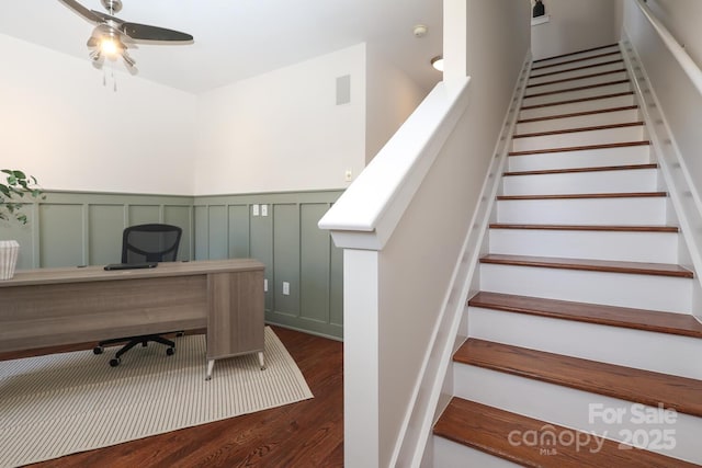 interior space with ceiling fan, a decorative wall, wood finished floors, visible vents, and wainscoting